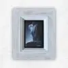 Side-lit oil painting of a female torso in cool greys and blue against black, in a whitewashed frame, by Julie Tugwell.